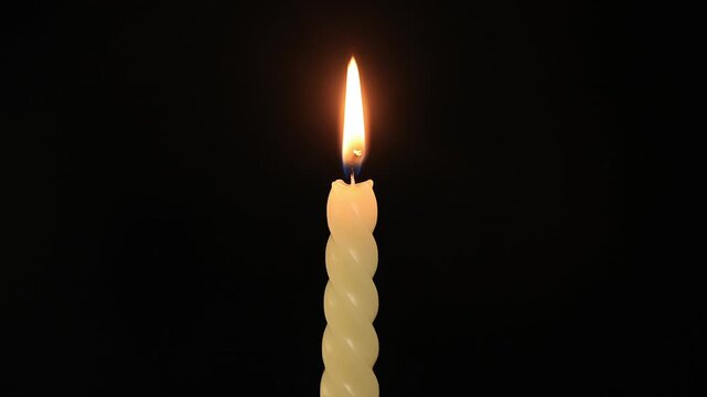 A candle in a conceptual time-lapse burning down and melting on black background; 4K 60FPS slow motion