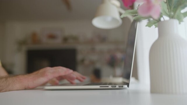 Close-up view of male hands opening a laptop and beginning to type on the keyboard, working from a bright and modern home office with soft, natural light in the background