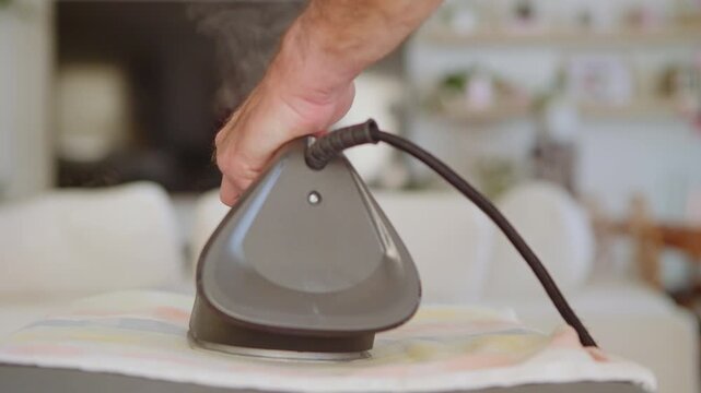 Close-up of a distracted man ironing clothes. He forgets the hot iron face-down on the fabric and leaves the room, creating a dangerous domestic fire hazard and safety risk.