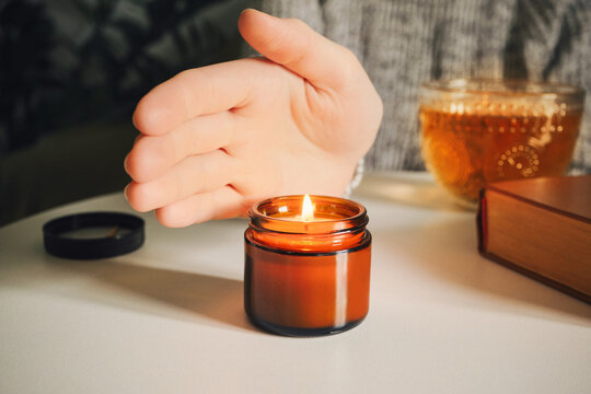 Woman warming her hand over candle with tea and book