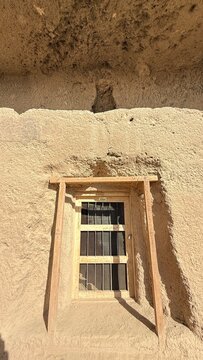 View of a protected cave niche with a barred opening carved into a sandy cliff at the Buddha of Bamyan site in Bamyan Afghanistan. The opening is set within rock-cut walls with sunlit shadows.