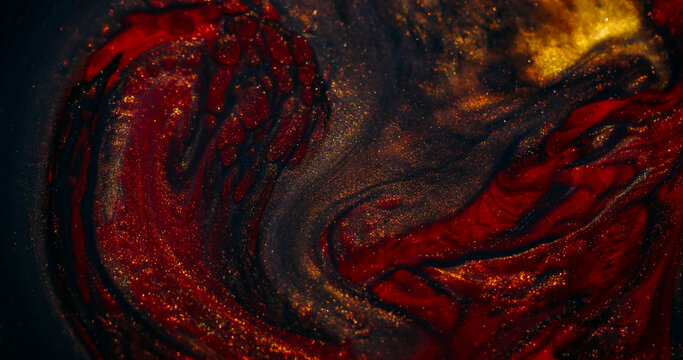 Ink spill. Sparkling fluid. Defocused yellow red colorful glitter mix acrylic texture floating on abstract art background.