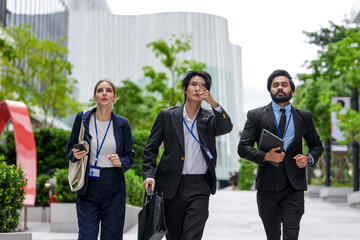 Fototapeta premium Three young business professionals wearing conference badges advance together down the corporate promenade along a sunlit walkway between contemporary corporate (frame 146)