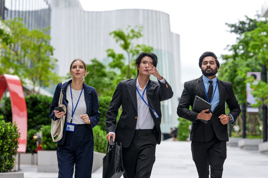 Three young business professionals wearing conference badges advance together down the corporate promenade along a sunlit walkway between contemporary corporate (frame 146)