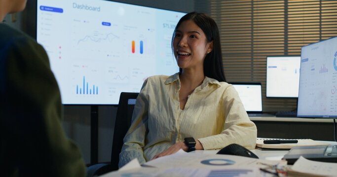 Two overworked Asian businesswomen talking and learning late indoors. A professional entrepreneur giving advice, explaining tech expertise, and reviewing corporate training.