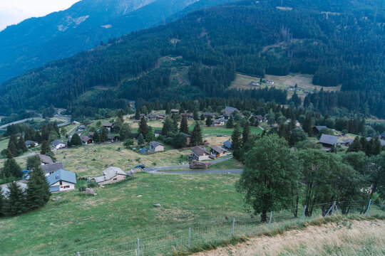 Small houses are scattered across a green mountain hillside surrounded by dense conifer forest and meadows in Switzerland. Peaceful alpine countryside represents rural living, mountain settlement, agr