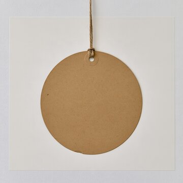 Blank round kraft gift tag hanging from a twine string, featuring a recycled paper texture for a packaging label mockup with copy space