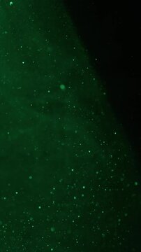 Vertical video. Particles texture. Glitter green background. Defocused natural color vibrant sparkling paint water on dark black bokeh abstraction.