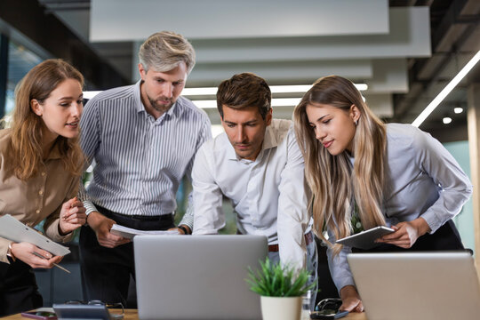 Business people discussing work together using a tablet and laptop taking notes in a modern office