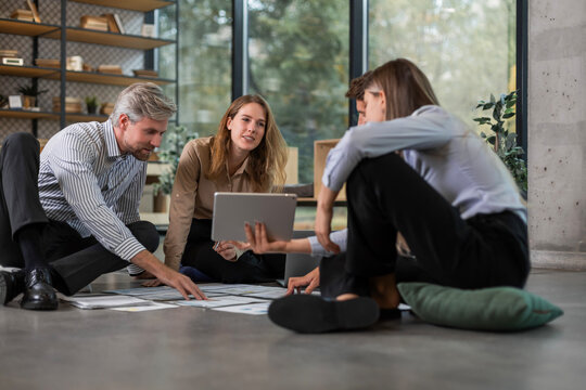 Business people looking at project plan laid out on floor, discussing new project plan in modern office.