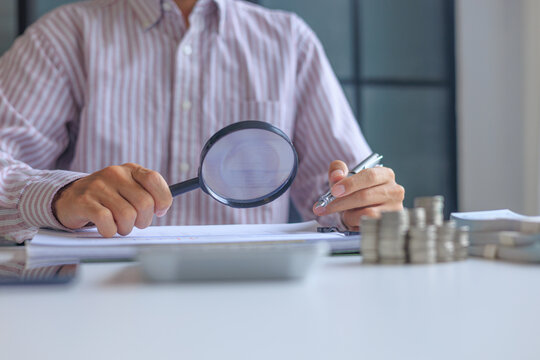 A person using magnifying glass to conduct a financial audit and bookkeeping review. financial analysis and forensic accounting to prevents leaks and invoicing errors.