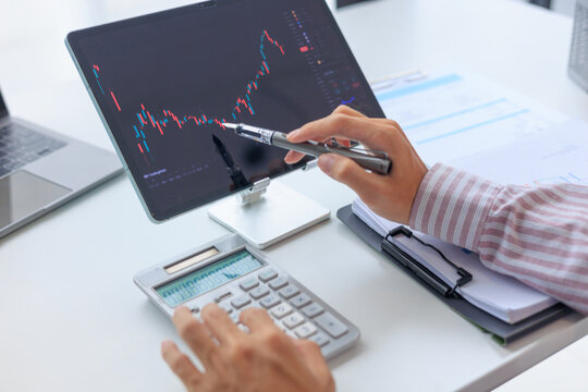 Businessman working on screen monitoring stock market and using calculator to analyze data and investment portfolio trends.
