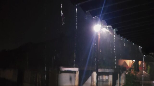 Streetlight illuminating a rainy night over a closed commercial storefront with a shutter, capturing a moody urban downpour and a quiet, dark city street atmosphere.