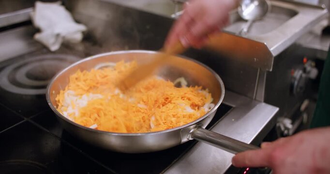 Frying meal. Cooking pan. Chef hand stirring shredded orange carrot with sliced onion on hot oil skillet preparing vegetable recipe.