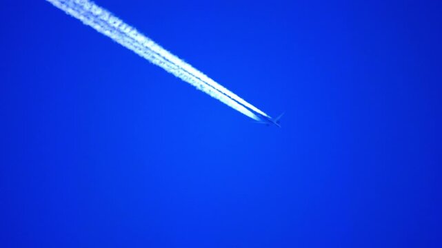 Airplane flying high in a clear blue sky leaving a long white contrail behind, high altitude view