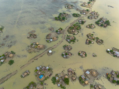 Rajshahi District, Bangladesh - 19 September 2026: Aerial view of a rural village submerged by severe monsoon flooding, with houses surrounded by murky floodwaters and a dirt road.
