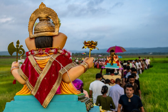 Kharsai, India - 19 September 2026: View of a procession carrying a Ganesha idol through a green field during the Ganesh Chaturthi festival with people walking behind.