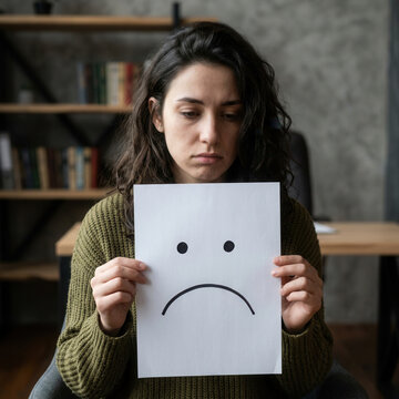 Young Woman Expressing Sadness Holding a Drawn Frowny Face Sad Emotion Representation