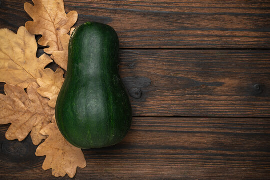 Green Squash with Autumn Leaves on Wooden Background: Seasonal Rustic Composition