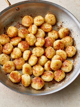 Large frying pan filled with small, round, golden-brown tater tots. the tots appear to be seasoned with herbs and spices, giving them a crispy texture.