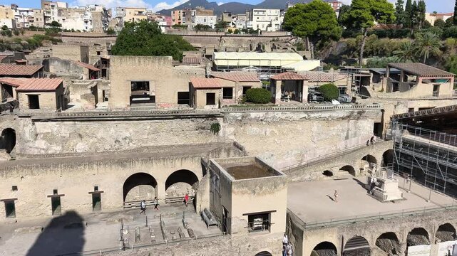 ERCOLANO, ITALY - SEPTEMBER 20, 2026: Panoramic view of the ancient Roman ruins of Herculaneum from above, with Mount Vesuvius in the background on a sunny day