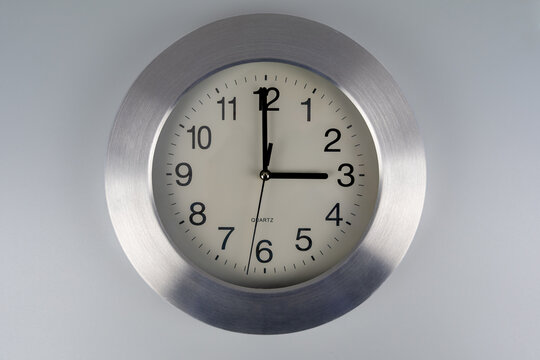 Time change: a large wall clock with a silver frame against a gray background, set to 3 o'clock.