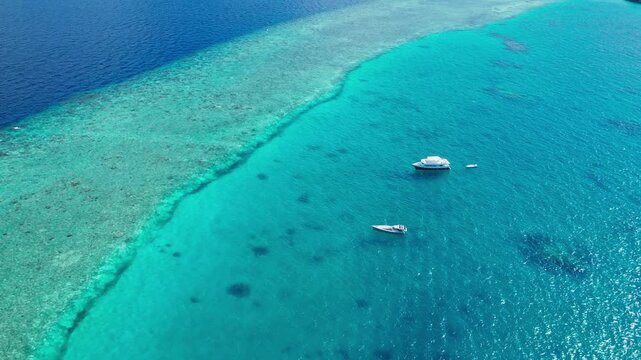A serene aerial view of a tropical island in the Maldives showcasing transparent water, sandy beaches, a vibrant blue sky, a boat, and a coral reef in bright light.