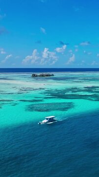 Aerial view of a boat gently floating on the tranquil, vibrant blue and green waters of a sunny Maldives reef, showcasing the serene beauty of a perfect holiday scene. Vertical video