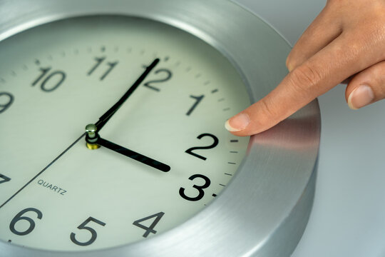 Woman's hand adjusting a wall clock from 3 to 2 for the autumn daylight saving time change to fall back one hour