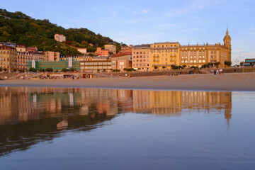 Obraz premium Sunset over Zurriola beach with city reflection on wet sand, San Sebastian, Basque Country, Spain