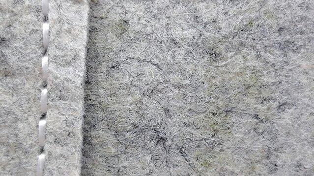 Close-up of light gray felt fabric texture with a vertical stitched seam and visible fiber details textile