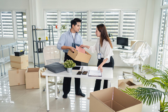 Young asian business coworkers packing and carrying cardboard boxes together during office relocation and moving into a new workplace
