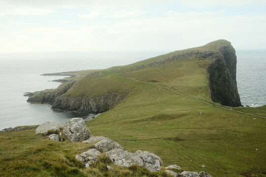 View of Neist Point Lighthouse on rugged cliffs with grassy slopes and rocky terrain overlooking the Atlantic Ocean, Isle of Skye, Scotland, United Kingdom.