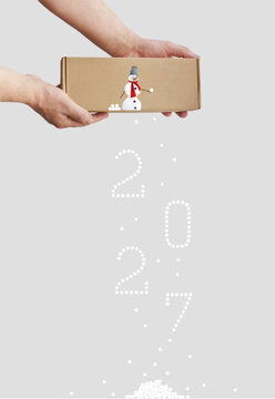 New year 2027 forecast financial concept with snowman throwing snowballs from cardboard box as upcoming economic changes, snowball effect or winter holiday marketing budget metaphor. Vertical image