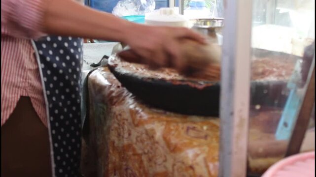 Food vendor is grinding peanuts and palm sugar using a mortar and pestle to make delicious peanut sauce dressing
