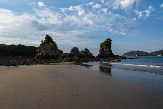 Scenic sandy beach with dramatic rock formations, calm sea and reflections under a blue sky.