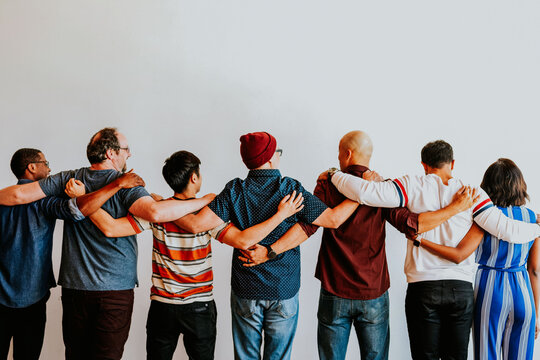 Diverse group of people standing with arms around each other, facing away from the camera.