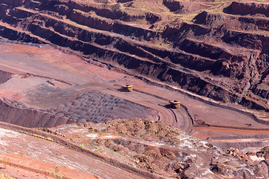 View of the Pilbara iron ore mine with large haul trucks operating on terraced red earth levels in Newman, Western Australia, Australia.