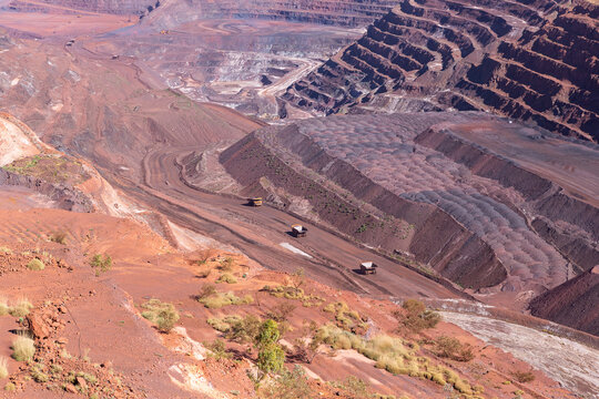 View of the expansive open-pit iron ore mine in the Pilbara region with large haul trucks navigating the terraced landscape in Newman, Western Australia, Australia.