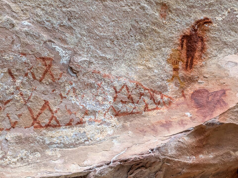 View of ancient petroglyphs and pictographs on a sandstone rock wall, featuring anthropomorphic figures and geometric patterns in red pigment, Moffat County, Colorado, United States.