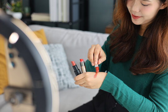 Young woman holding lipstick tubes options, beauty blogger reviewing makeup cosmetics products close up.