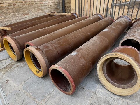 Row of weathered metal pipes with cream-colored coating, heavy industrial equipment outdoors