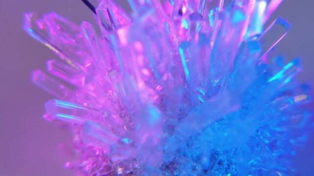 A real crystal. The grown crystal rotates on an illuminated turntable. A scientific experiment and chemical study. A beautiful background or screensaver. Pink and blue.