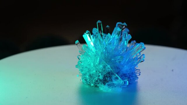 A real crystal. The grown crystal rotates on an illuminated turntable. A scientific experiment and chemical study. A beautiful background or screen. Iridescent colors: blue, purple, green