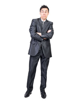 Full body of surprised young male employee with dark hair in elegant suit standing against with crossed arms and looking away with doubt