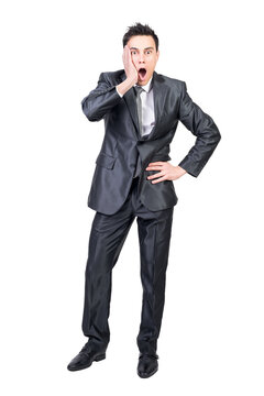 Full body of astonished young male manager in formal clothes touching cheek and looking at camera with opened mouth with hand on waist.