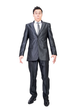 Full length of serious young male manager in formal suit and tie with dark hair looking at camera with astonishment