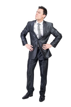 Full body of confident young businessman with dark hair in classy suit and tie with hands on waist and looking away with concentration