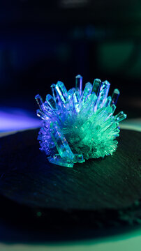 A mysterious, magical, genuine crystal. A grown crystal on a rotating, illuminated stand. A scientific experiment and chemical study. A beautiful background or screensaver. Blue and green.