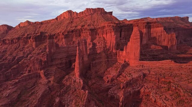 Warm evening light bathes towering sandstone spires and rugged desert canyons during a sweeping aerial flight near Moab Utah